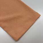 Close-up of soft peach-colored knit fabric, showcasing fine texture and smooth finish, ideal for clothing and fashion accessories.