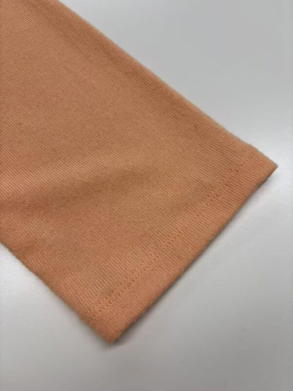 Close-up of soft peach-colored knit fabric, showcasing fine texture and smooth finish, ideal for clothing and fashion accessories.