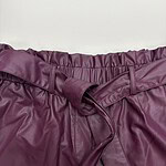 Close-up of a burgundy leather skirt with an elastic waistband and a tied belt, showcasing trendy fashion for women.