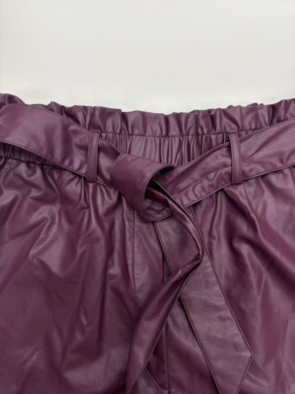 Close-up of a burgundy leather skirt with an elastic waistband and a tied belt, showcasing trendy fashion for women.
