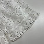 Close-up of white eyelet lace fabric with intricate heart-shaped cutouts and embroidered details, perfect for fashion and home decor.