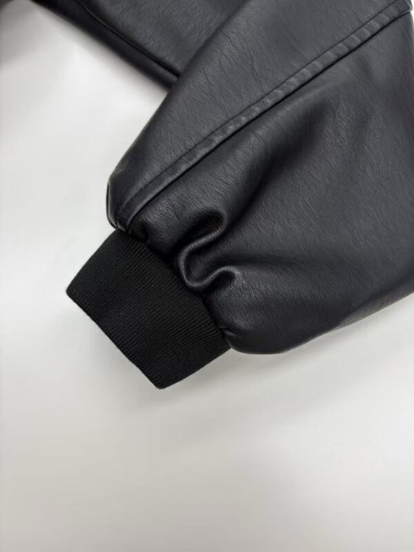Close-up of a black leather jacket sleeve with ribbed cuff, showcasing high-quality material and craftsmanship.