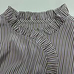 Close-up of a women's blouse with vertical purple, white, and black stripes, featuring ruffled details around the neckline and front.
