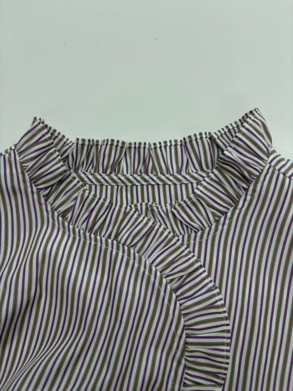 Close-up of a women's blouse with vertical purple, white, and black stripes, featuring ruffled details around the neckline and front.