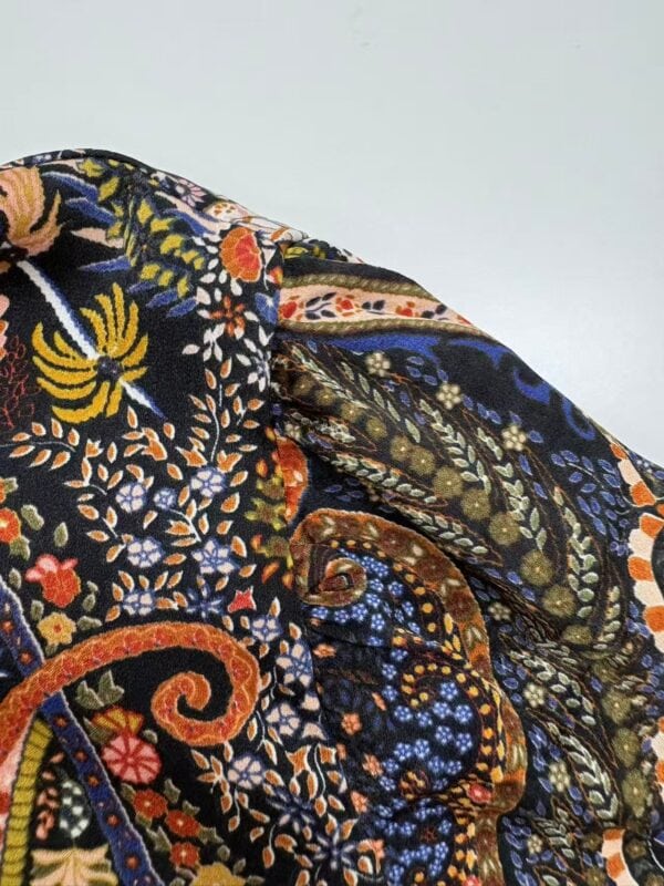 Close-up of vibrant embroidered fabric with floral and paisley patterns in blue, orange, yellow, and green on black background.