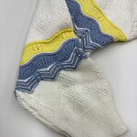 Close-up of a knitted sock featuring a zigzag pattern in blue, yellow, and white colors, showcasing detailed stitching and vibrant design.