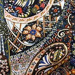 Close-up of intricate embroidered textile featuring floral and geometric patterns in vibrant colors.