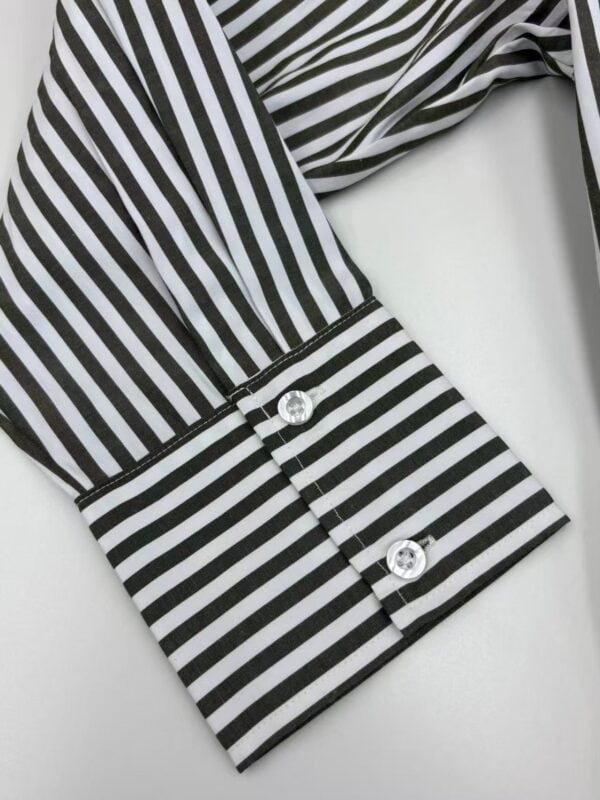 Close-up of a black and white striped shirt cuff with two shiny buttons, showcasing stylish fashion details.
