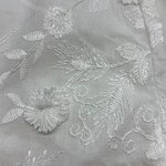 Close-up of white fabric with intricate floral embroidery, showcasing detailed stitching and delicate design suitable for high-end fashion or wedding dresses.