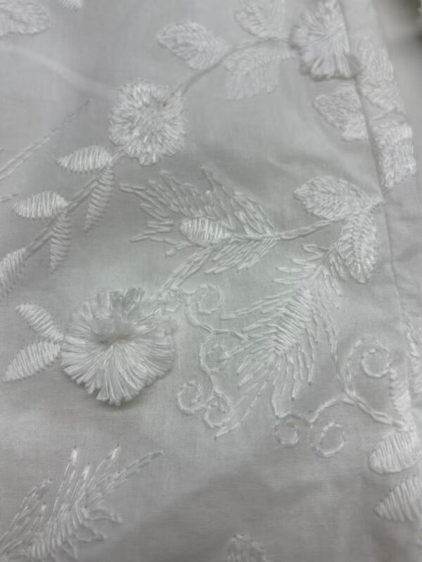 Close-up of white fabric with intricate floral embroidery, showcasing detailed stitching and delicate design suitable for high-end fashion or wedding dresses.