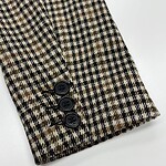 Close-up of a blazer sleeve with a classic houndstooth pattern in brown, black, and beige, featuring three black buttons at the cuff.