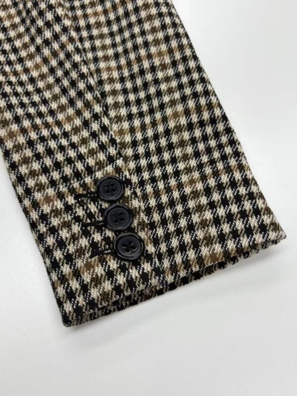 Close-up of a blazer sleeve with a classic houndstooth pattern in brown, black, and beige, featuring three black buttons at the cuff.