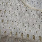Close-up of a cream-colored perforated fabric top with intricate cut-out patterns and a rounded neckline, perfect for stylish summer wear.