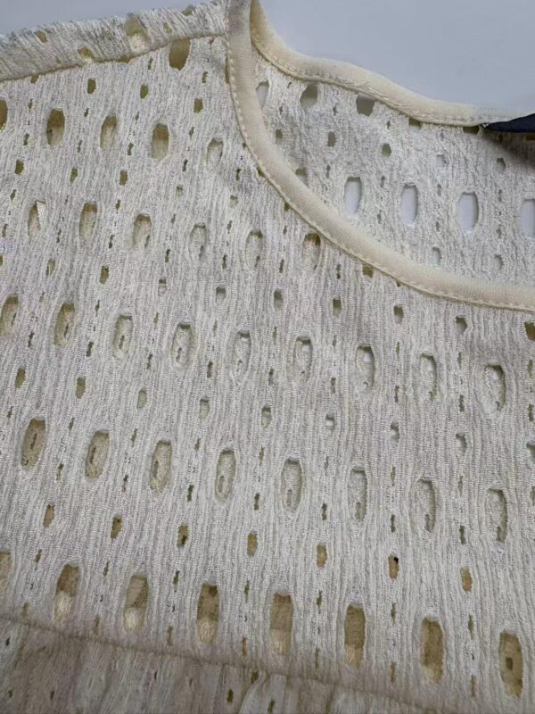 Close-up of a cream-colored perforated fabric top with intricate cut-out patterns and a rounded neckline, perfect for stylish summer wear.