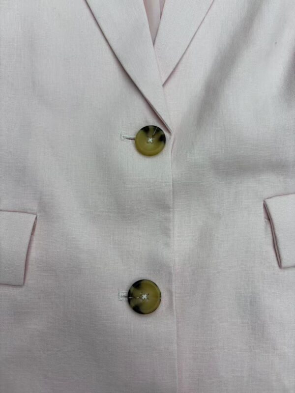 Close-up of a beige blazer featuring two large, shiny buttons and a tailored lapel, perfect for stylish professional or casual wear.