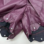 Close-up of a purple leather jacket with silver studs and black fabric lining, showcasing trendy fashion details.