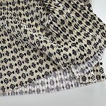 Close-up of fabric with black geometric diamond and stripe pattern on a beige background, showcasing detailed textile design.