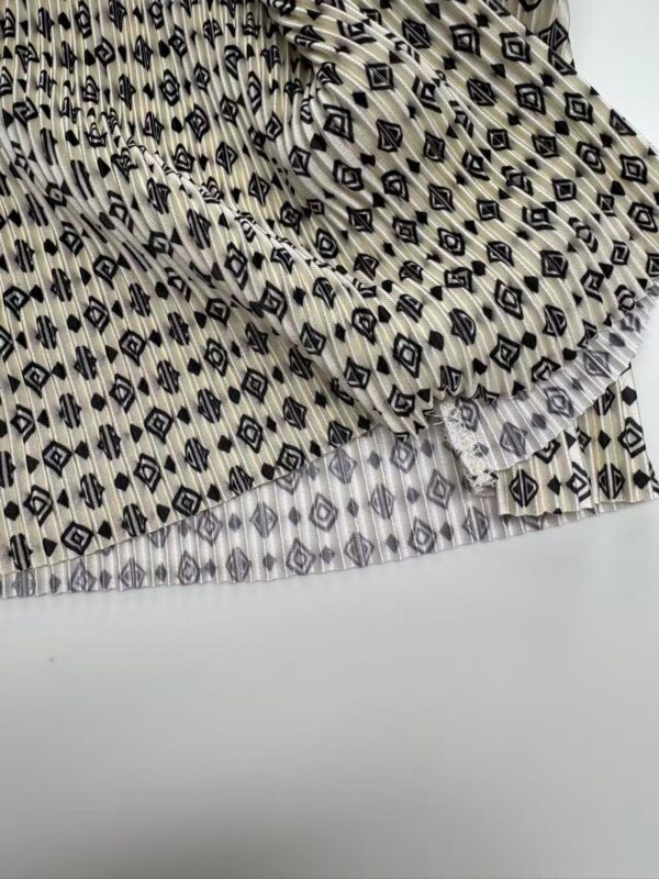 Close-up of fabric with black geometric diamond and stripe pattern on a beige background, showcasing detailed textile design.