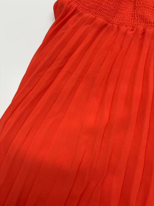 Close-up of a bright red pleated skirt with a high elastic waistband, showcasing fine pleats and smooth fabric texture, perfect for fashion and style.