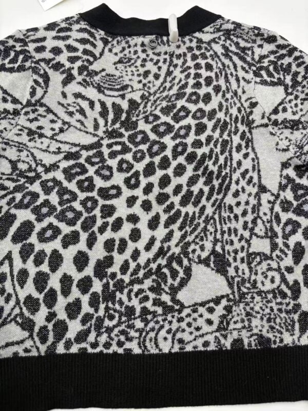 Close-up of a stylish women's sweater with a bold leopard print pattern in black and white, featuring a round neckline and ribbed hem.