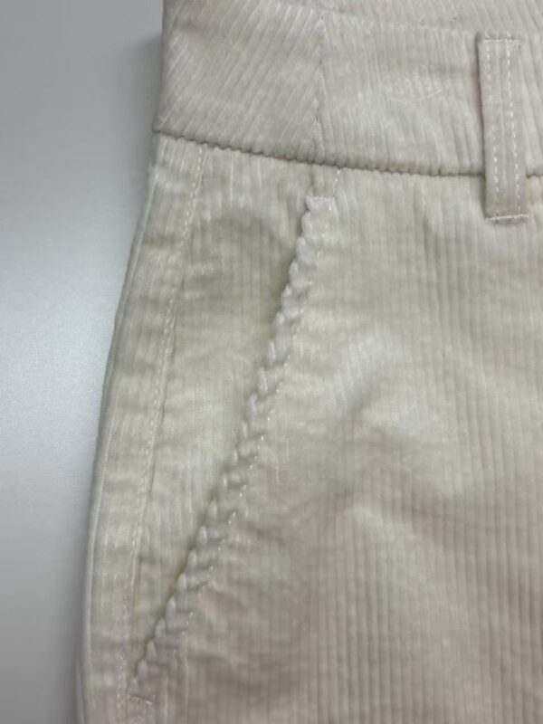 Close-up of cream-colored corduroy pants showing textured fabric and detailed stitching on the pocket area.