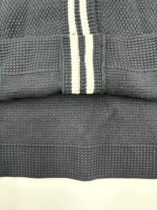Detailed close-up of black knit fabric with textured patterns and white stripe detail, showcasing quality material and craftsmanship.