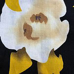 Close-up of a floral fabric pattern featuring a large white flower with yellow accents on a black background, ideal for fashion and textile projects.