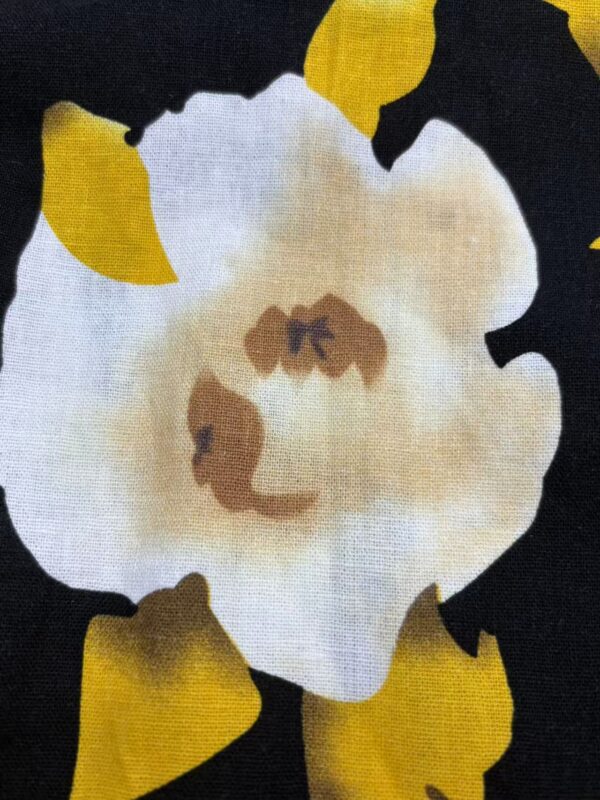 Close-up of a floral fabric pattern featuring a large white flower with yellow accents on a black background, ideal for fashion and textile projects.