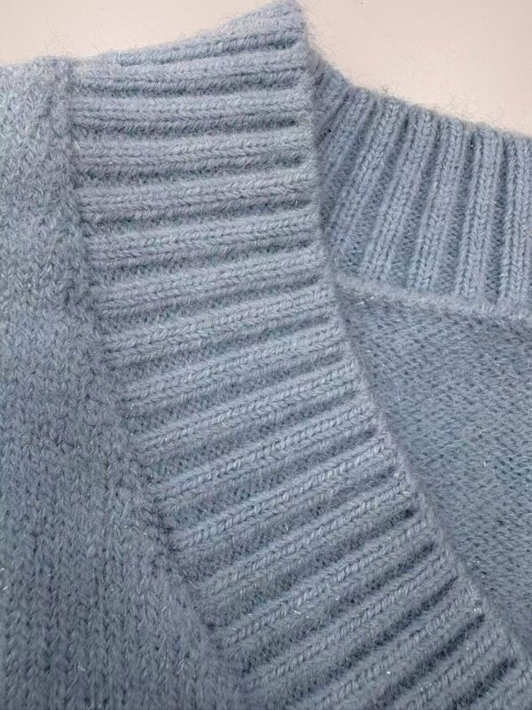 Close-up of a light gray knitted sweater with ribbed collar and textured pattern, perfect for casual or formal wear.