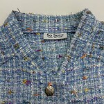 Close-up of a women's tweed jacket with multicolored threads and a decorative button, showcasing high-quality fabric and stylish design.