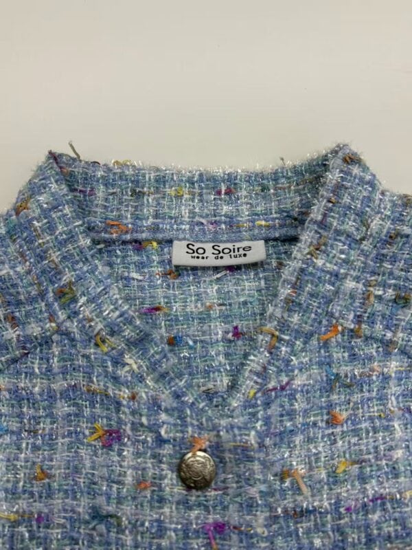 Close-up of a women's tweed jacket with multicolored threads and a decorative button, showcasing high-quality fabric and stylish design.