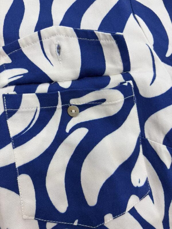 Close-up of a stylish shirt with a bold blue and white leaf pattern, featuring a buttoned pocket and collar detail, perfect for fashion-forward outfits.