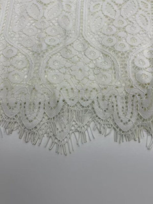 Close-up of intricate white lace fabric with floral and geometric patterns, perfect for fashion and bridal wear.