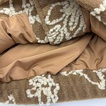 Close-up of a plush brown fleece blanket with cream floral patterns and satin lining, perfect for winter warmth and home decor.