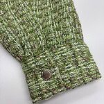 Close-up of a green tweed fabric sleeve with a decorative button, showcasing textured woven pattern and stylish design.