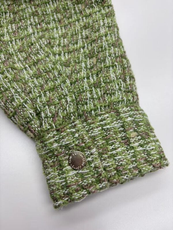 Close-up of a green tweed fabric sleeve with a decorative button, showcasing textured woven pattern and stylish design.