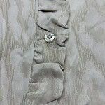 Close-up of beige fabric with gathered ruffle detail and a single shiny button, showcasing fine textile craftsmanship.