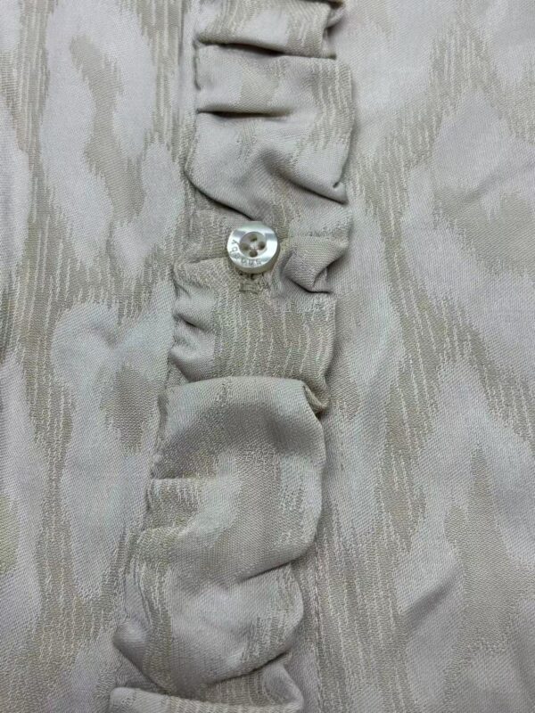 Close-up of beige fabric with gathered ruffle detail and a single shiny button, showcasing fine textile craftsmanship.