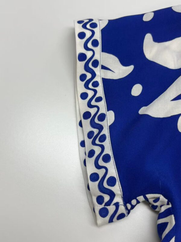 Close-up of a blue fabric with white abstract and decorative patterns, showcasing detailed design and craftsmanship.