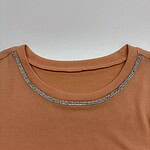 Close-up of a peach-colored top featuring a rhinestone-embellished neckline, perfect for casual or semi-formal wear.