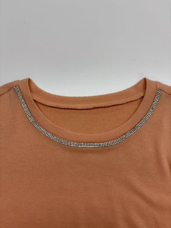 Close-up of a peach-colored top featuring a rhinestone-embellished neckline, perfect for casual or semi-formal wear.