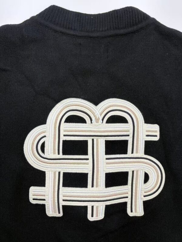 Close-up of a black sweater featuring a distinctive embroidered logo design in white and beige tones.