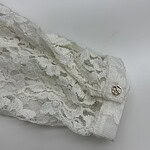 Close-up of white lace fabric with intricate floral patterns and a decorative button, perfect for fashion and bridal wear.