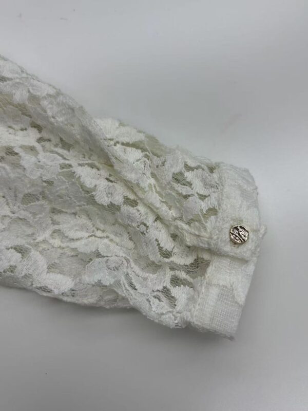 Close-up of white lace fabric with intricate floral patterns and a decorative button, perfect for fashion and bridal wear.