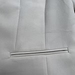 Close-up of a light gray suit jacket with a sleek, horizontal pocket and subtle stitching, showcasing high-quality tailoring and fabric.