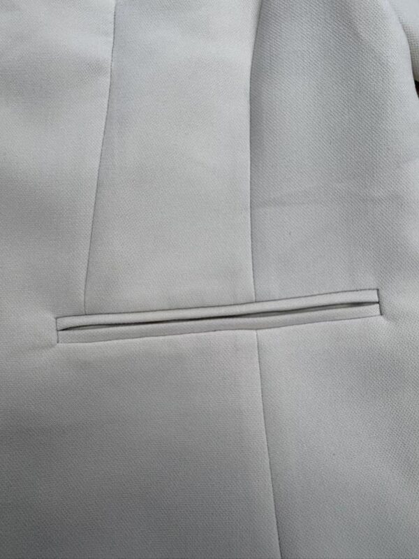 Close-up of a light gray suit jacket with a sleek, horizontal pocket and subtle stitching, showcasing high-quality tailoring and fabric.