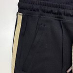 Close-up of black joggers featuring a gold stripe along the side, elastic waistband, and zippered pocket, perfect for casual or athletic wear.