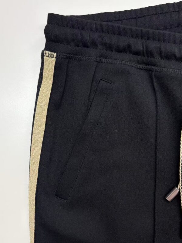 Close-up of black joggers featuring a gold stripe along the side, elastic waistband, and zippered pocket, perfect for casual or athletic wear.