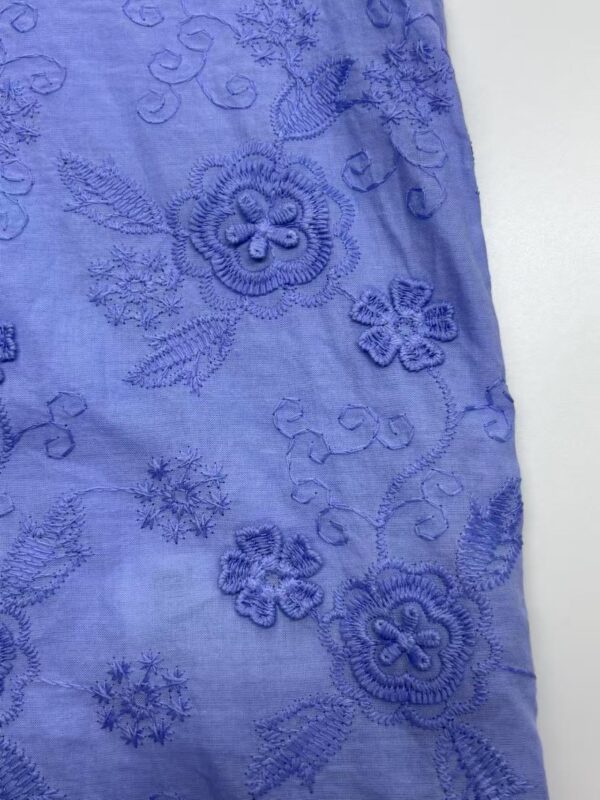 Close-up of blue fabric with intricate floral embroidery, showcasing detailed stitching and textured design, ideal for fashion or home decor.