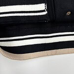 Close-up of black and beige striped knitwear fabric with gold button details, showcasing high-quality craftsmanship and stylish design.